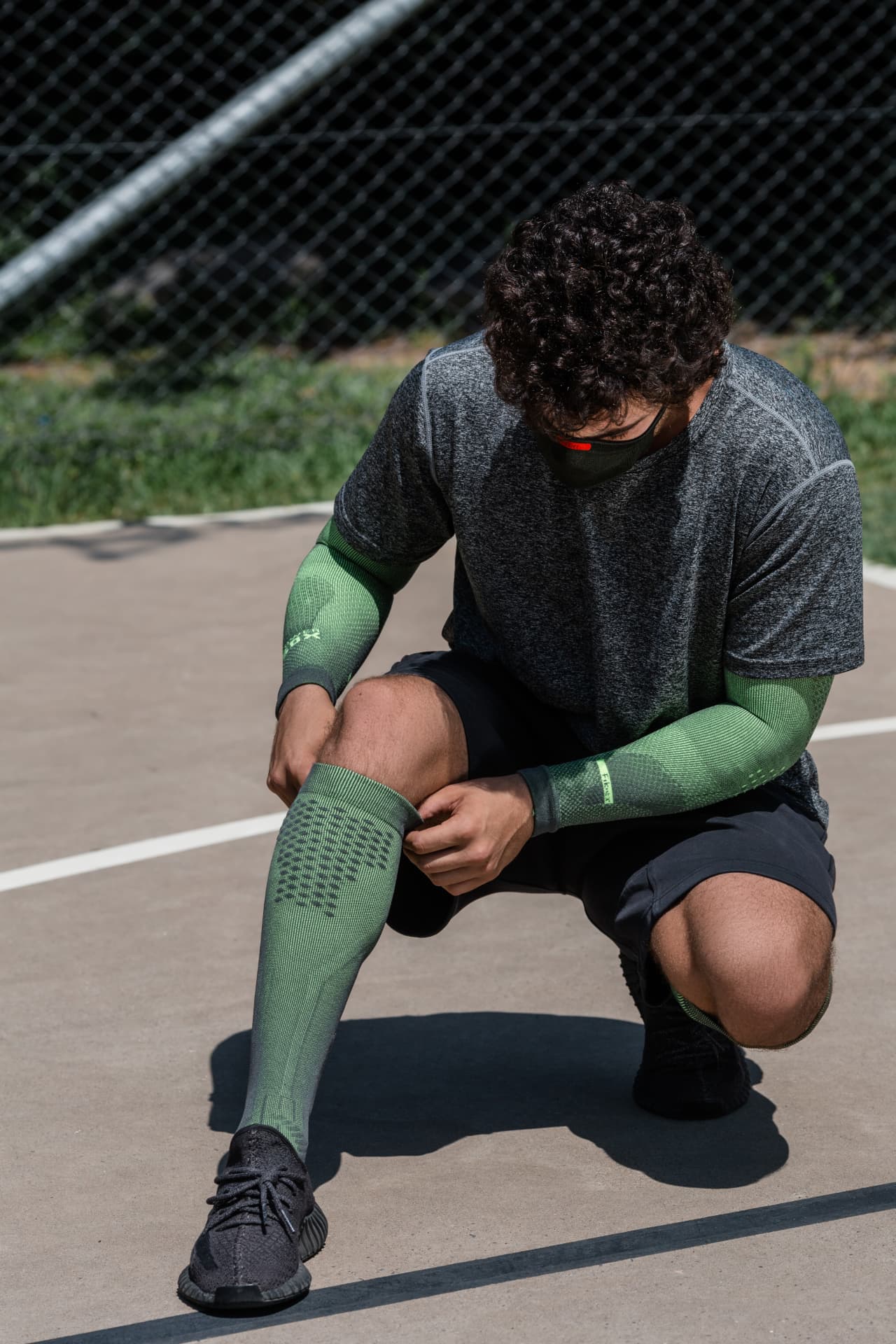 Athlete adjusting green KNIT knee-high compression socks on an outdoor court