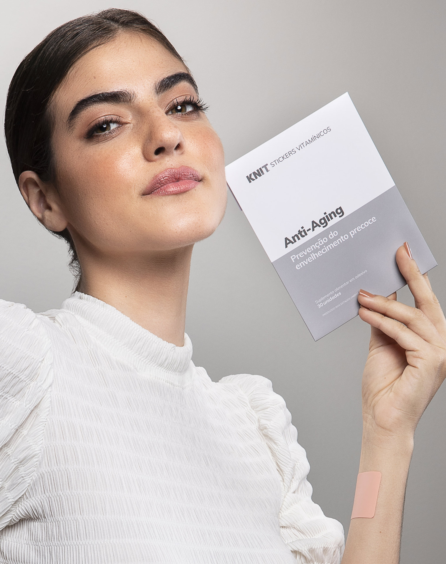 Model holding an Anti-Aging KNIT vitamin patch pack against a grey background